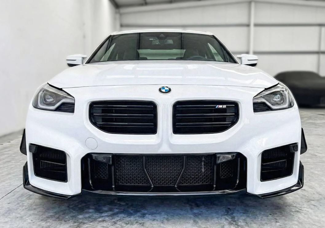 Fehér BMW G87 M2 elölről stúdióban, a lökhárítóba szerelt fekete védőhálóval