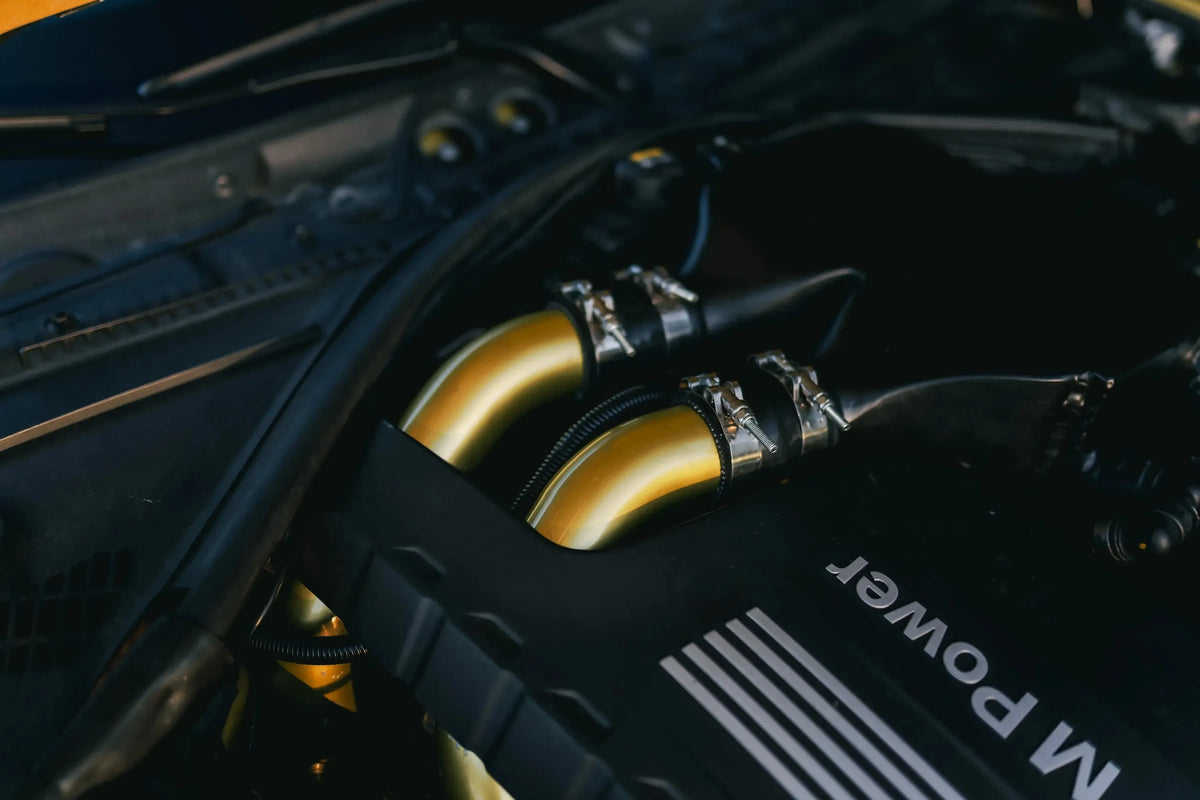 Installed gold-colored charge pipes in a BMW M3/M4 S55 engine bay, close-up