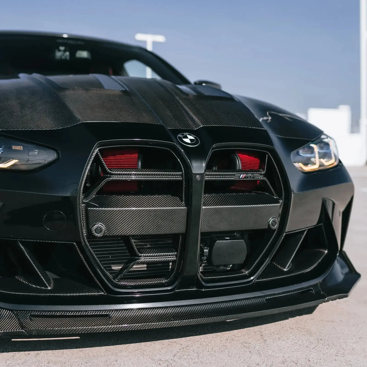 Black BMW G82 M4, low front three-quarter view, with red Front mount intake filters behind the grille