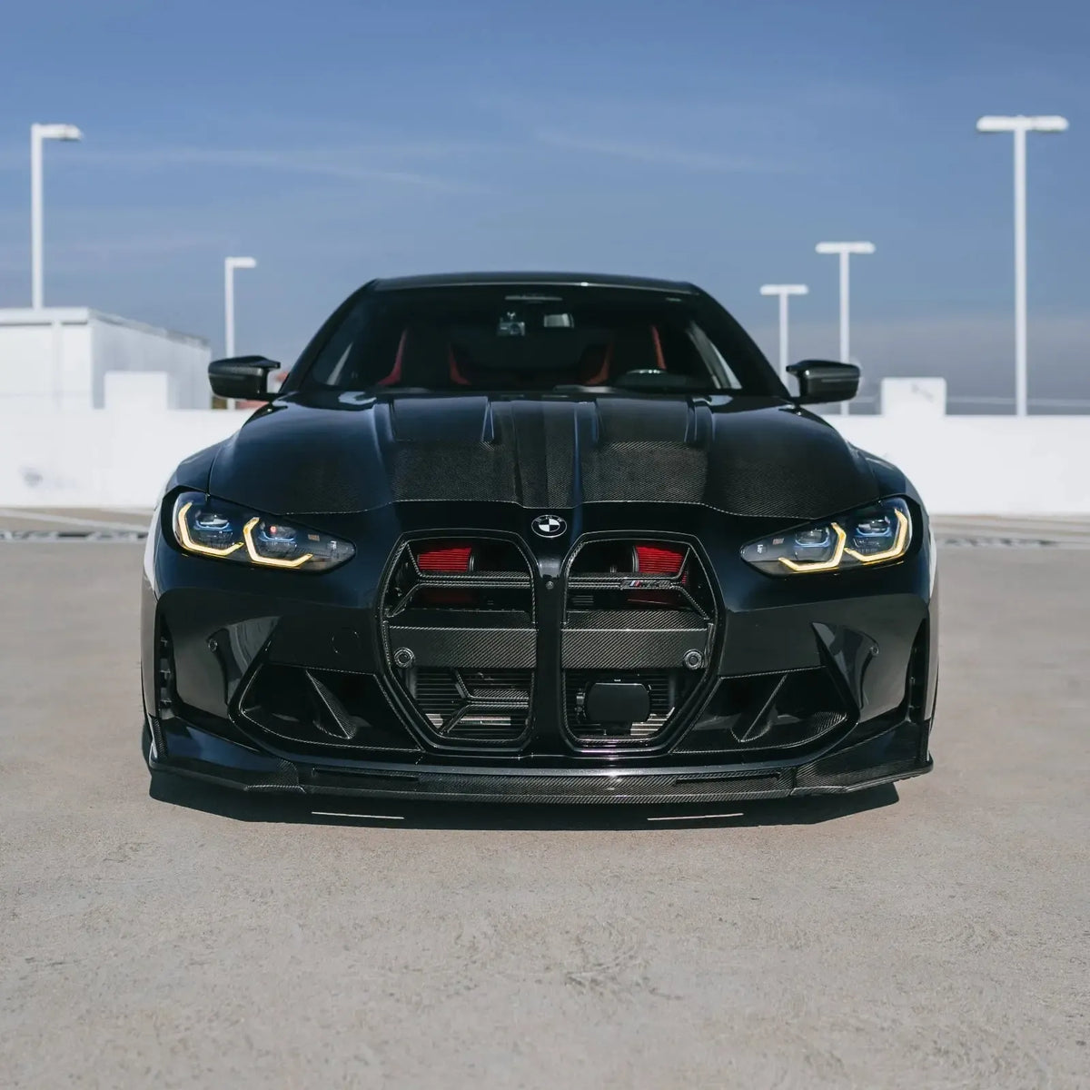 Black BMW G82 M4 from the front on a rooftop parking lot, with red Front mount intake filters behind the grille