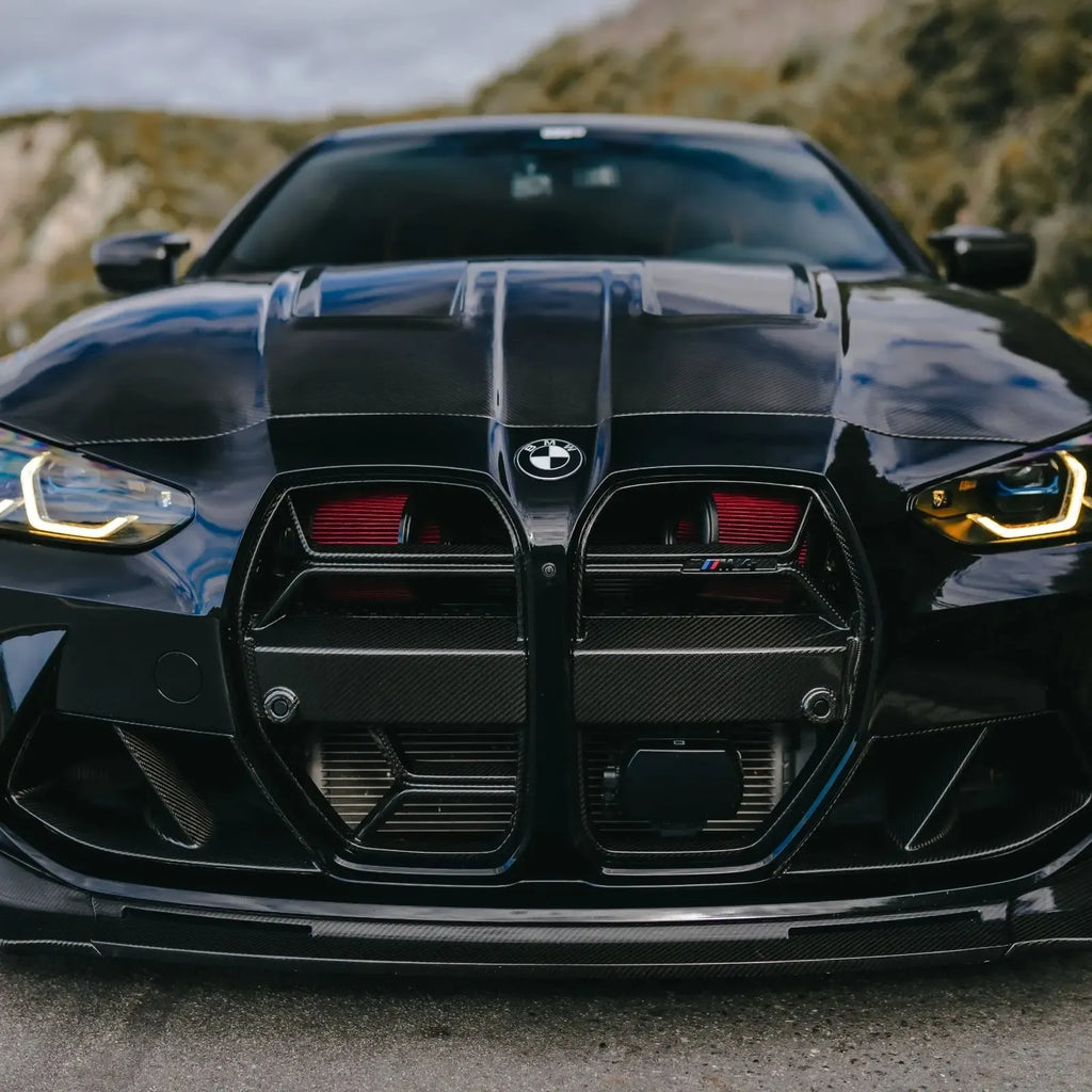 Front of a black BMW G82 M4, close-up, hills in the background, with red Front mount intake filters