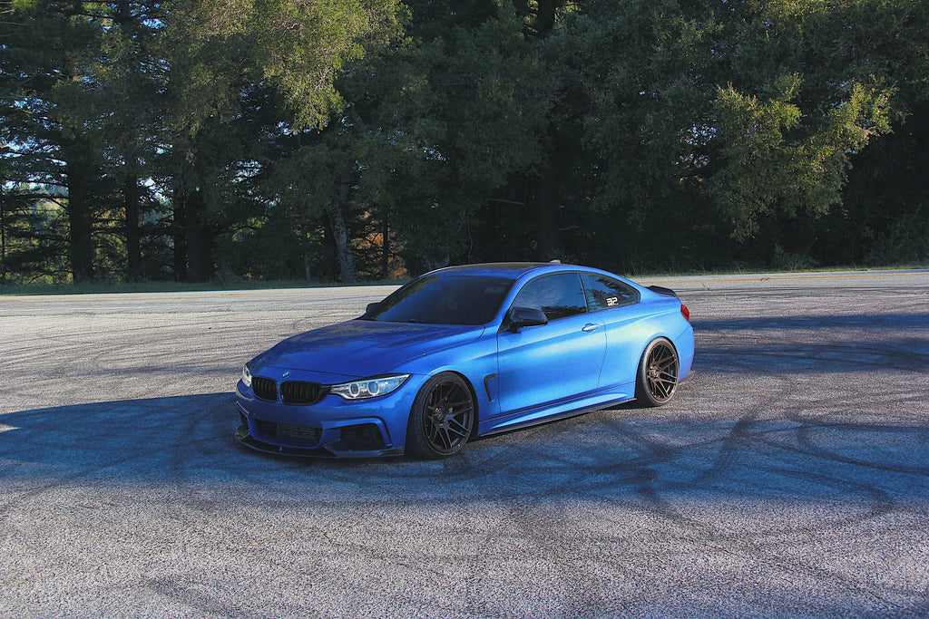 Kék BMW F32 távolabbról, első háromnegyed nézetben, carbon első koptatóval (MP Style)