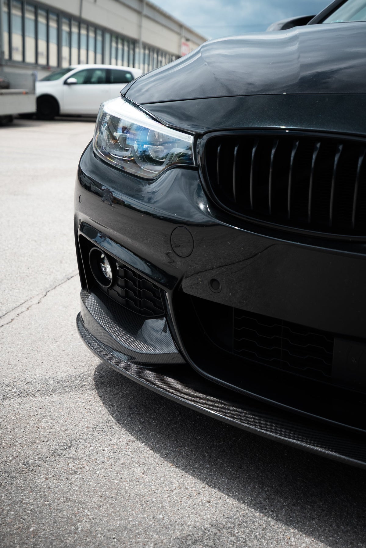 Fekete BMW F32 első lökhárítójának sarka közelről, felszerelt carbon első koptatóval (MP Style)