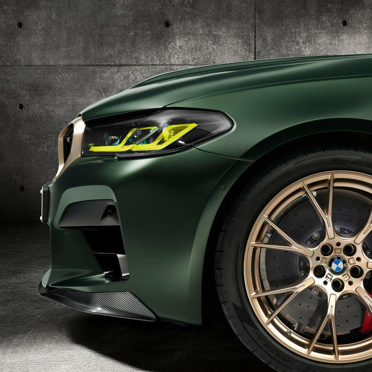 Close-up of a green BMW F90 M5 CS LCI front corner: yellow DRL, carbon front lip, gold wheel (CS Style)