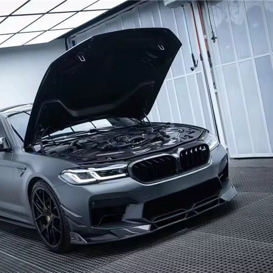Gray BMW F90 M5 LCI right front three-quarter view, with open hood and carbon center lip