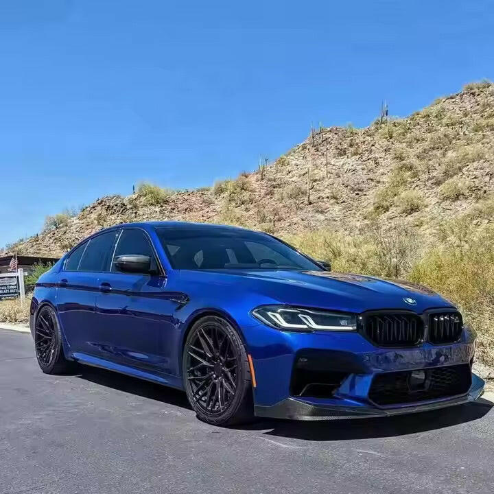 Blue BMW F90 M5 LCI front three-quarter view, with fitted carbon front lip (MP Style)