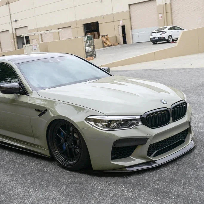 Gray-green pre-LCI BMW F90 M5 front three-quarter view, with fitted carbon front lip (V Style)