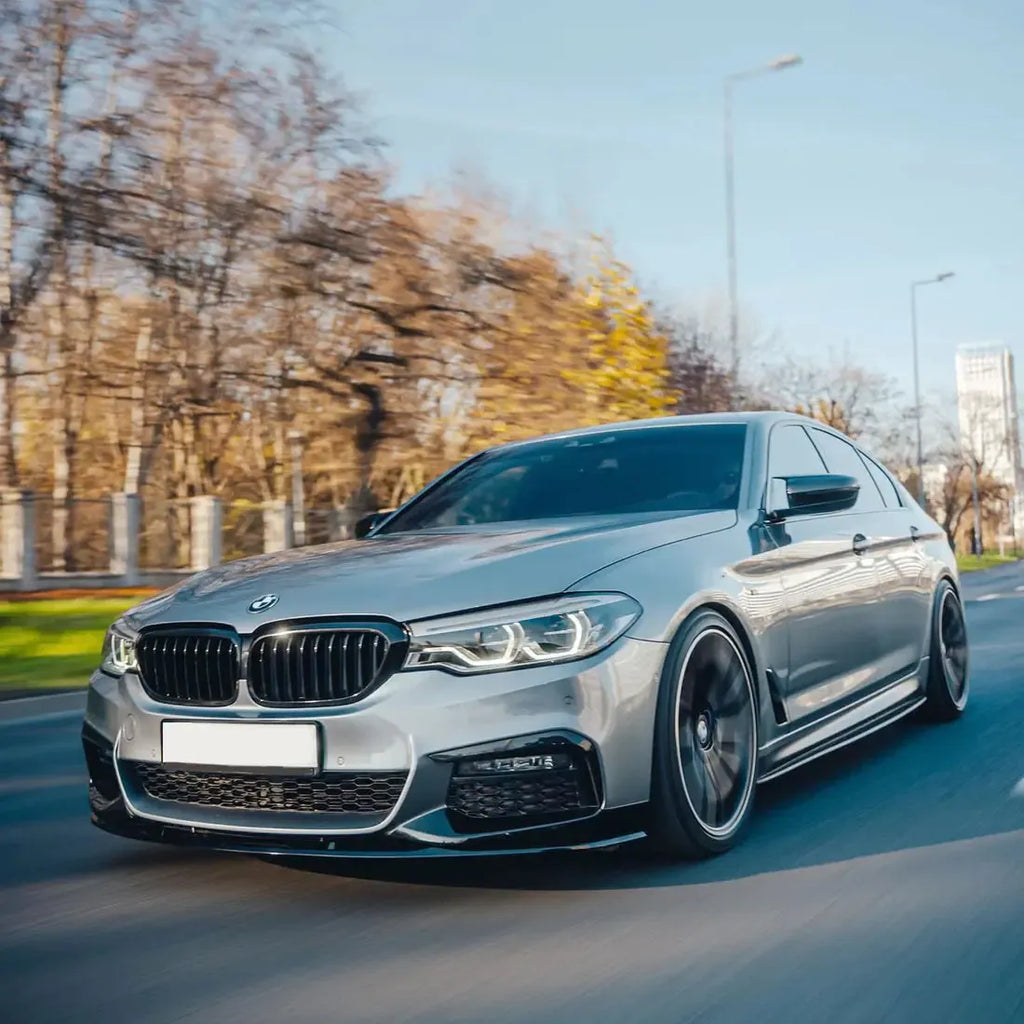 Silver pre-LCI BMW G30 M Sport while driving, front three-quarter view, with carbon front lip (MP Style)