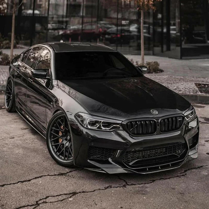 Black pre-LCI BMW F90 M5 front three-quarter view on a city street, with fitted carbon front lip (PM V2 Style)
