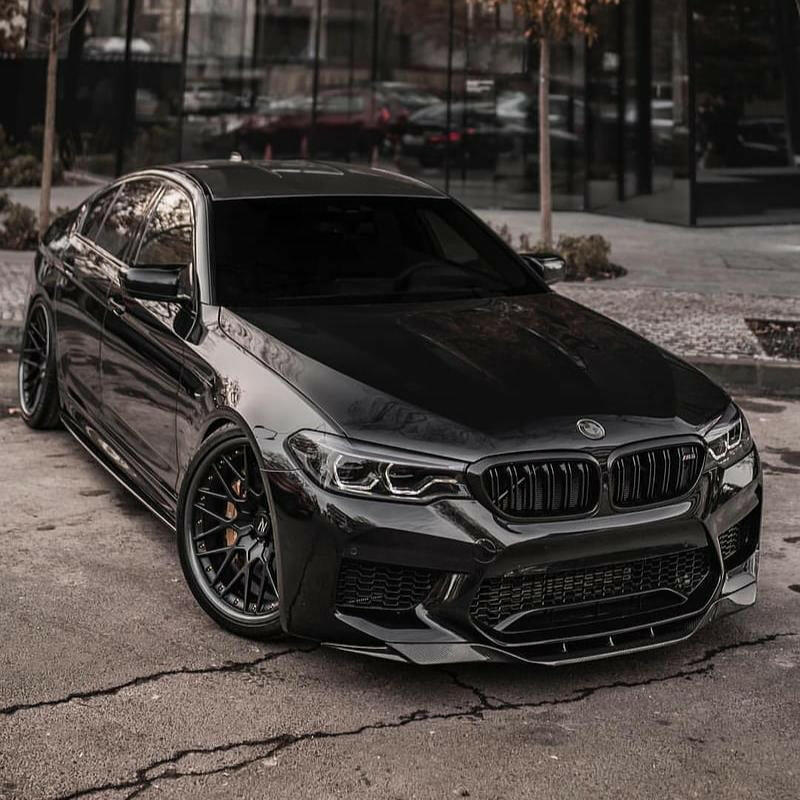 Black pre-LCI BMW F90 M5 front three-quarter view, with carbon hood and front lip (RKP Style)