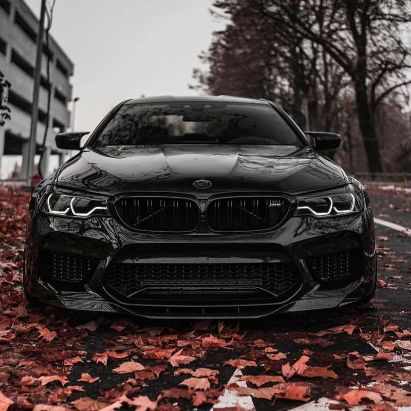 Black pre-LCI BMW F90 M5 head-on on autumn leaves, with fitted carbon front lip (RKP Style)