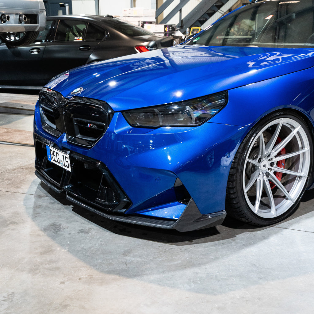 Kék BMW G90 M5 műhelyben, elölről 3/4 nézetben, carbon fiber első koptatóval (SQ Style V3)