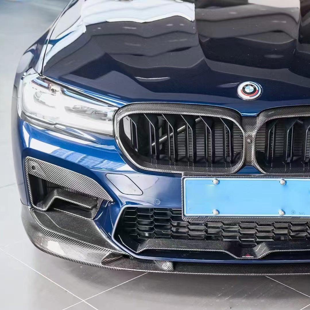 Kék BMW F90 M5 LCI első lökhárítója közelről, carbon ködlámpa keretekkel és koptatóval (PM Style)