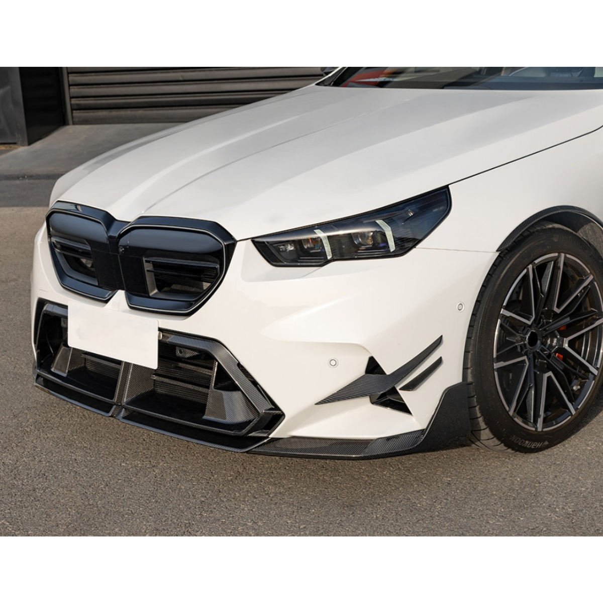 White BMW G90 M5 front three-quarter view, with ribbed carbon fiber center trim (SQ Style)