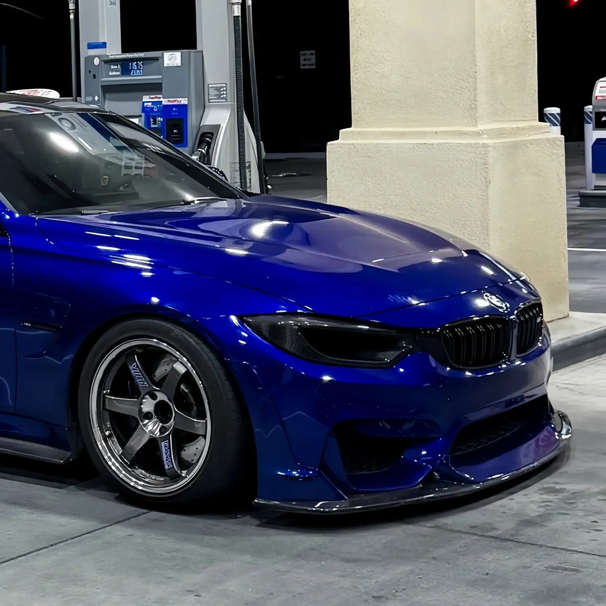 Kék BMW F80 M3 első 3/4-es nézetből éjjel, a fényszóró helyére szerelt carbon légbeömlővel