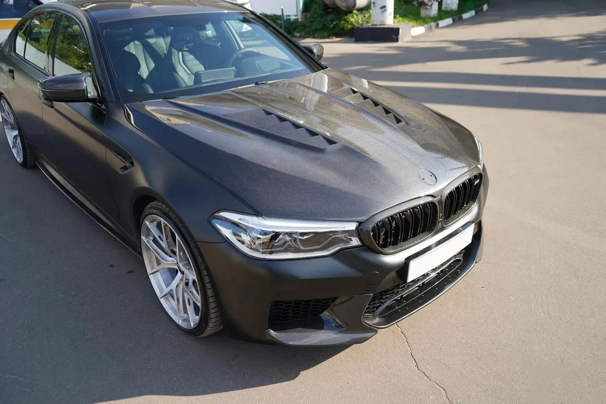 Szürke BMW F90 M5 első 3/4-es nézetben, szabadban, felszerelt szellőzős carbon motorháztetővel (GTR Style)