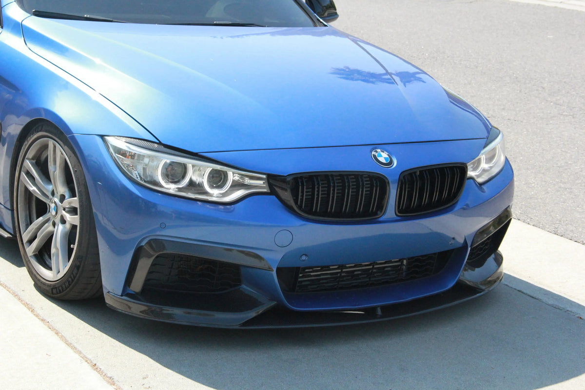 Kék BMW F32 coupé eleje közelről, a lökhárító légbeömlőin felszerelt carbon felső splitter párral