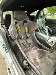 Szürke race seat sárga biztonsági címkékkel és fekete hevederekkel bmw m3 kipufogó és carbon fiber kipufogó rendszerhez