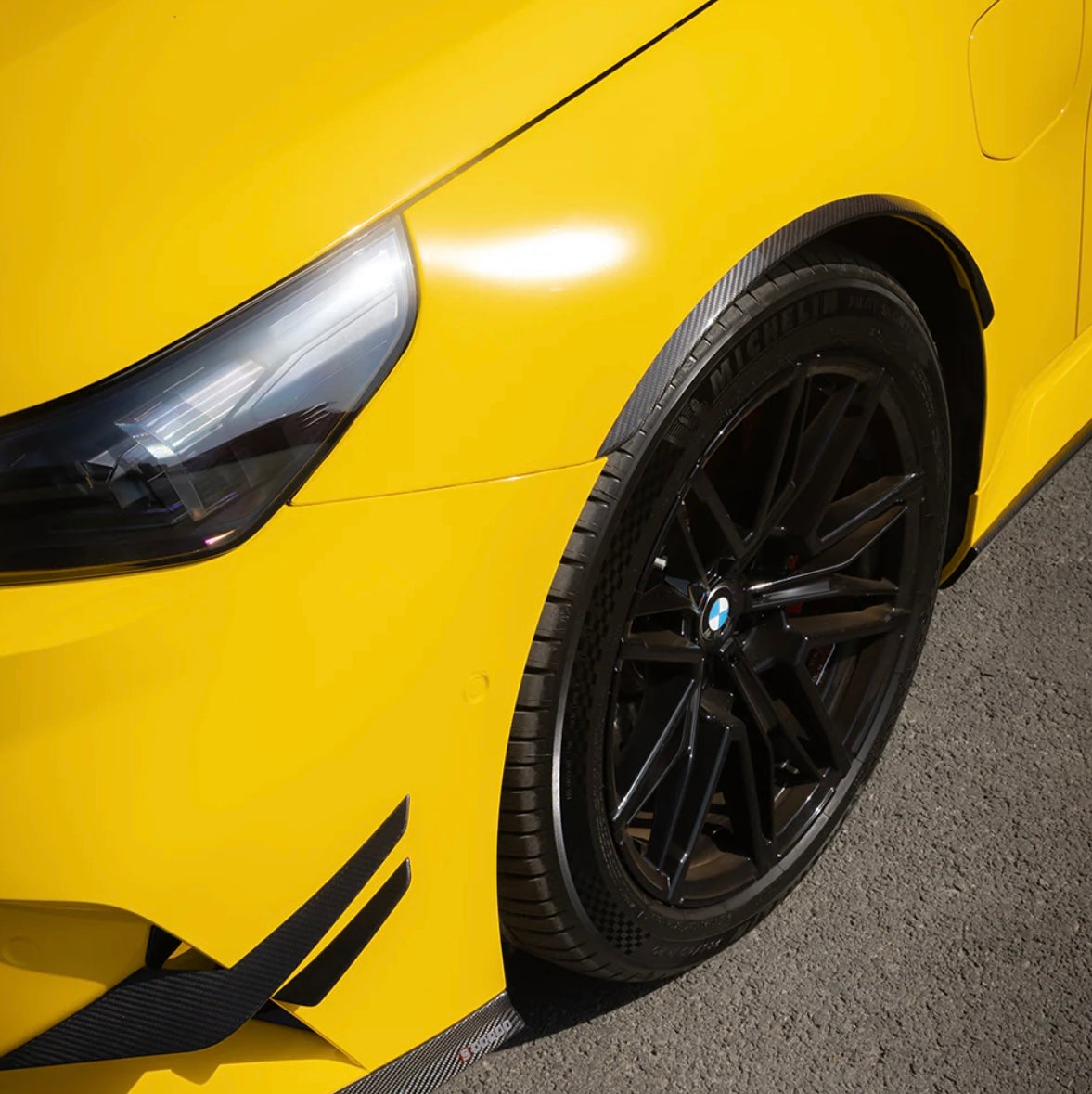 Sárga BMW G90 M5 első kerékíve közelről carbon kerékív díszléccel és canardokkal