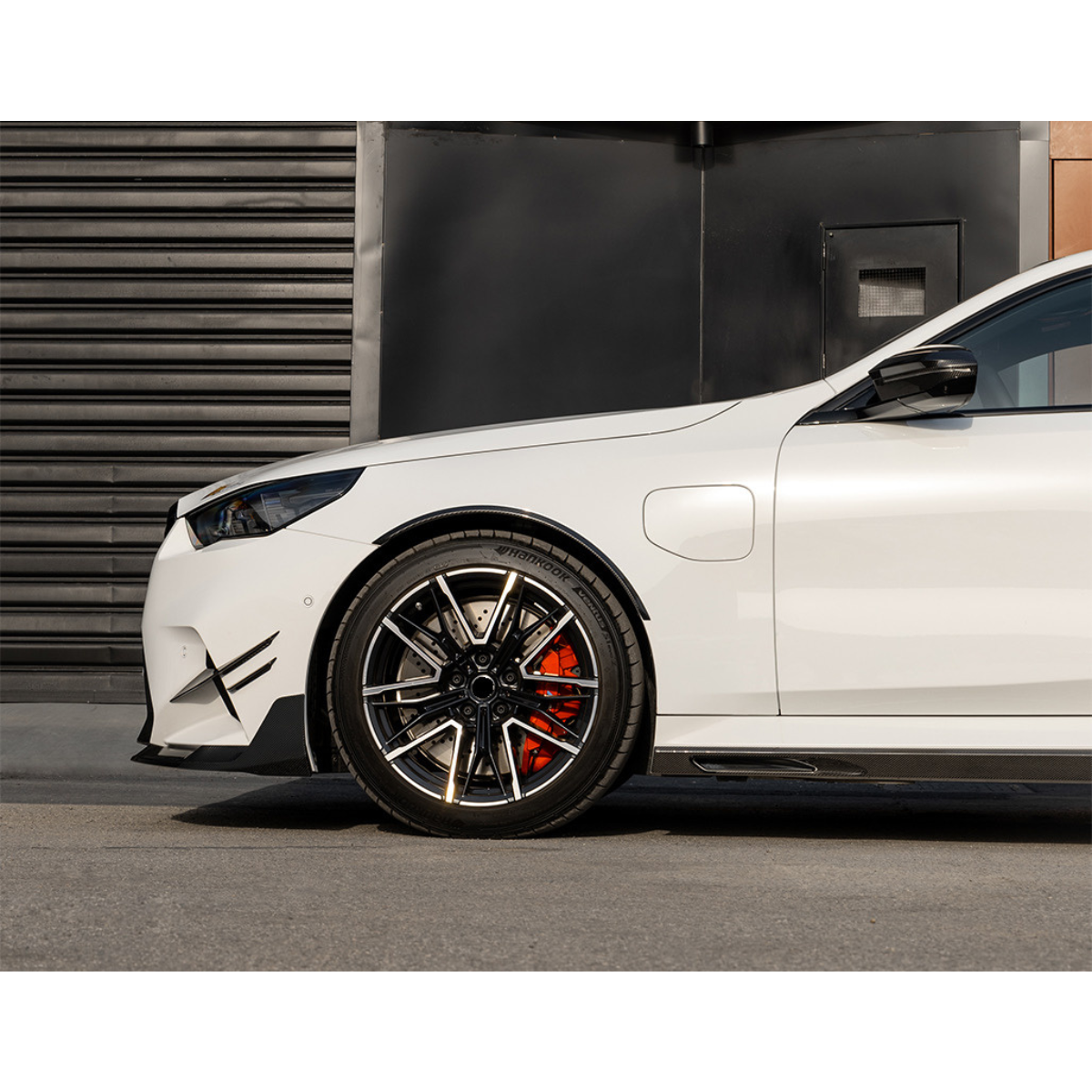 White BMW G90 M5 front from the side, with carbon wheel arch trim and canards