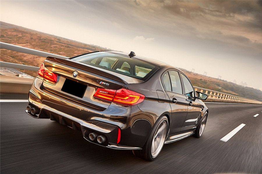Dark bronze pre-LCI BMW F90 M5 on the move, rear three-quarter view, with carbon spoiler (D3 Style)