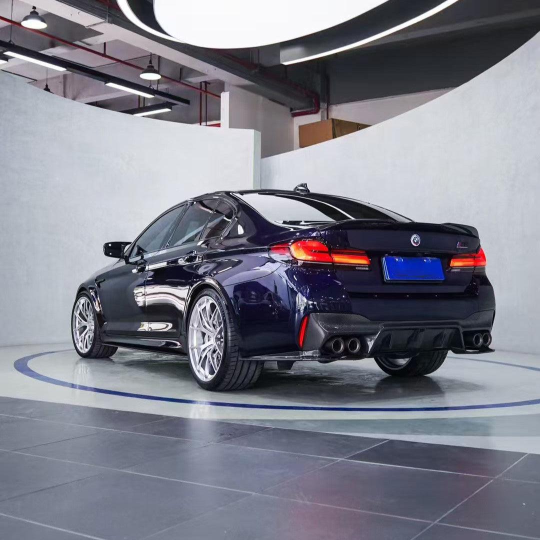 Dark blue LCI BMW F90 M5 in rear three-quarter view, with fitted carbon trunk spoiler (PM Style)