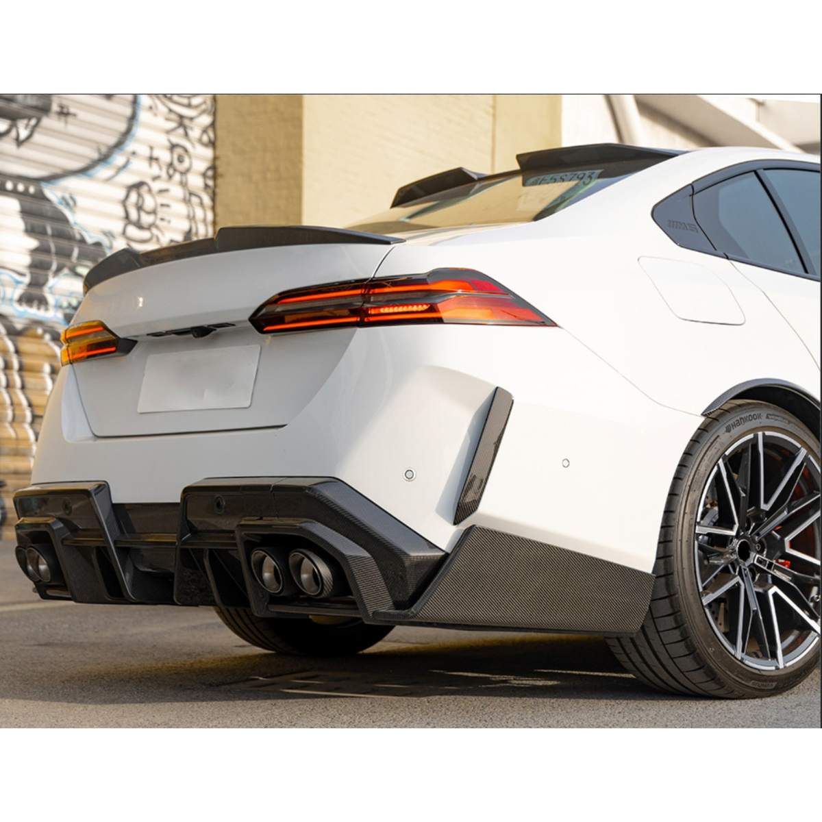 Rear three-quarter shot of a white BMW G90 M5 sedan with fitted carbon roof spoiler (SQ Style)