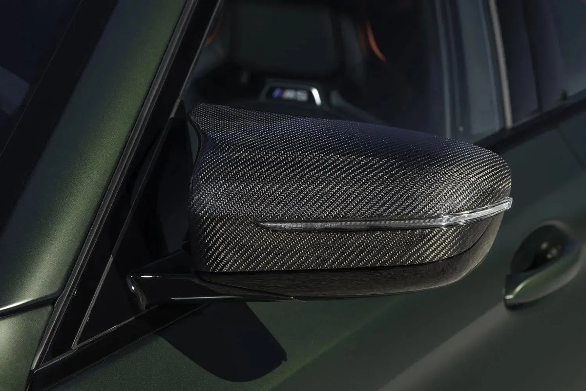 Close-up of a carbon mirror cap fitted to a matte green BMW F90 M5 mirror