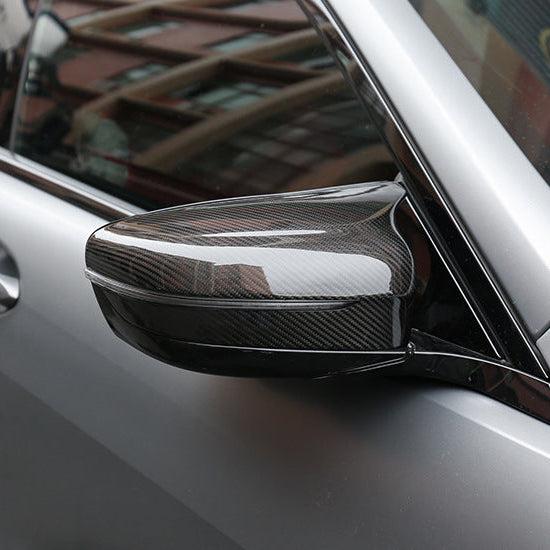 Close-up of a gray BMW F90 M5 side mirror, with fitted dry carbon mirror cap (PM Style)